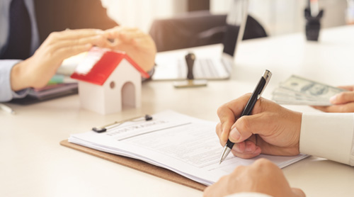 Signing papers at desk with small house model on it